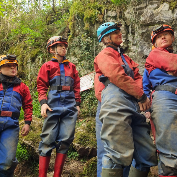 family looking exciting and nervous up at the hole they're about to climb into as they're about to go caving