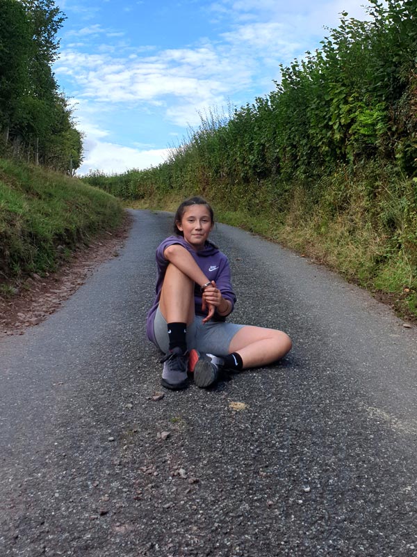 girl sat happily in the middle of the countryside road. She's just run up the hill and is content with her achievement