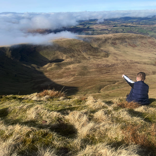 Boy sat on the top of a mountain pointing out at the view